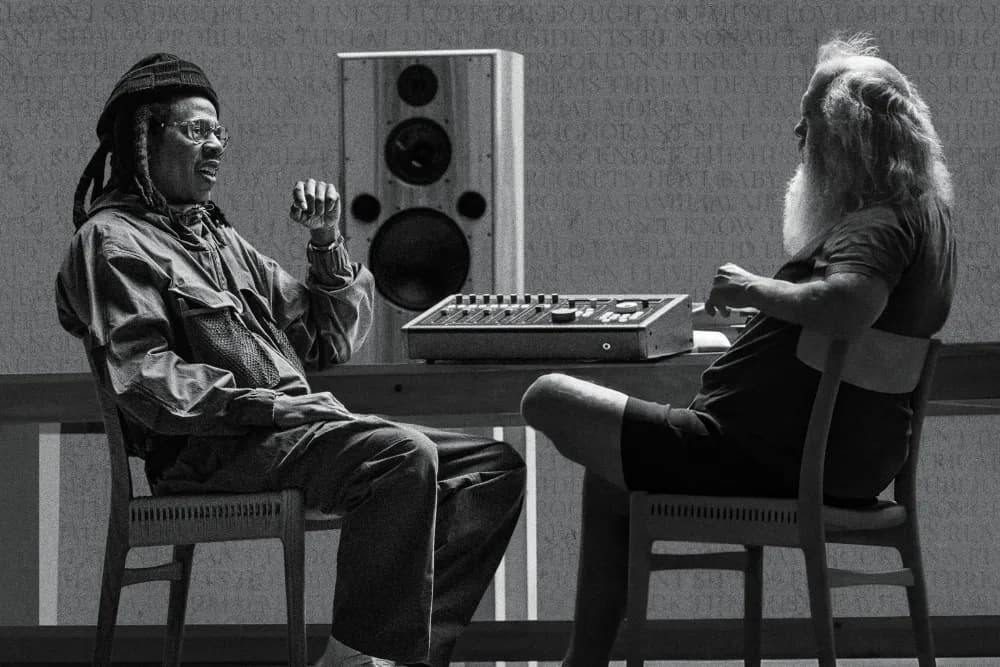 A black-and-white photograph of Jay-Z and Rick Rubin seated across from each other at a mixing desk, mid-conversation