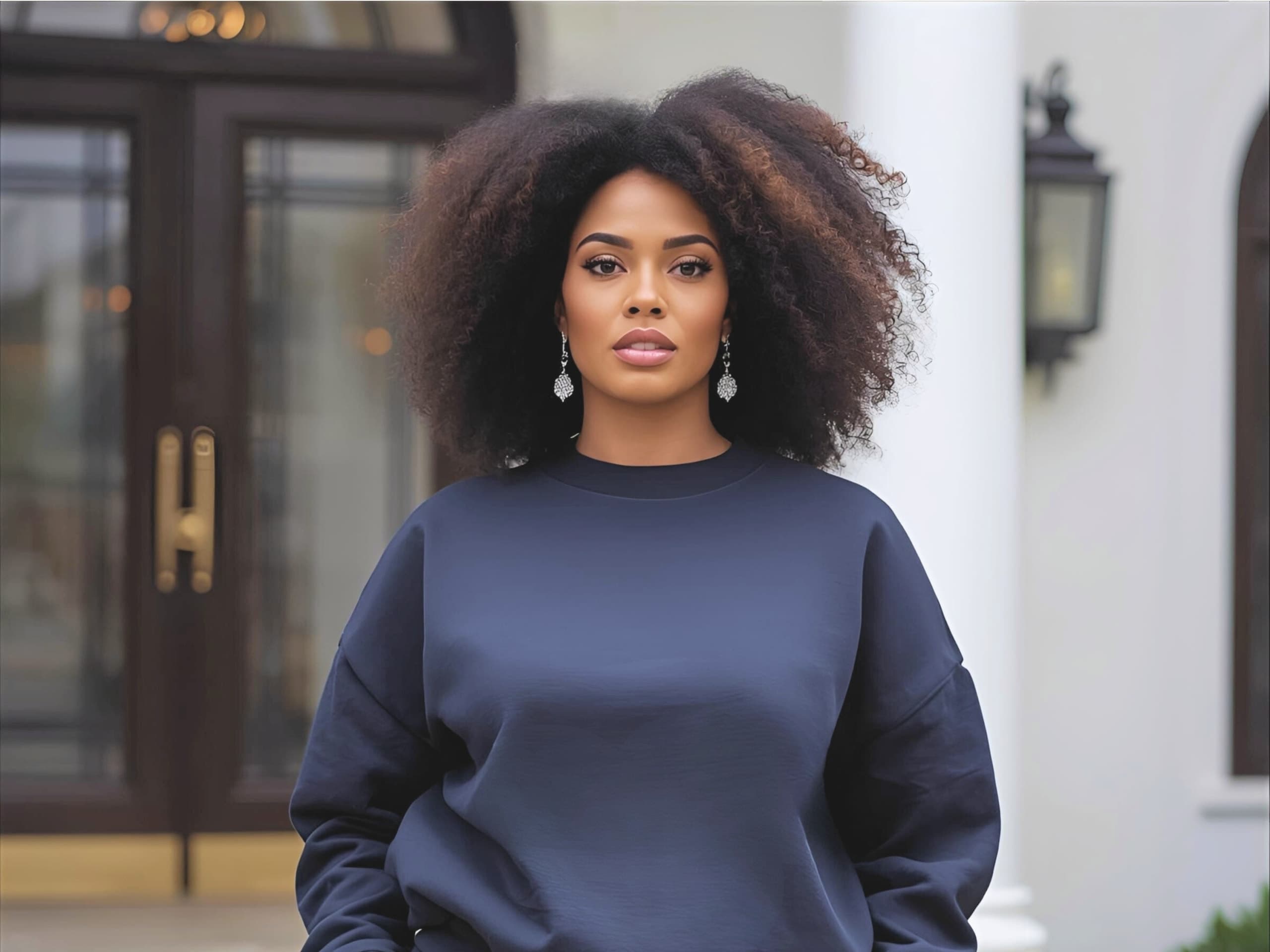 A woman in a simple navy sweatsuit standing poised on the steps of an elegant home, the contrast between the setting and her understated outfit doing quiet work.