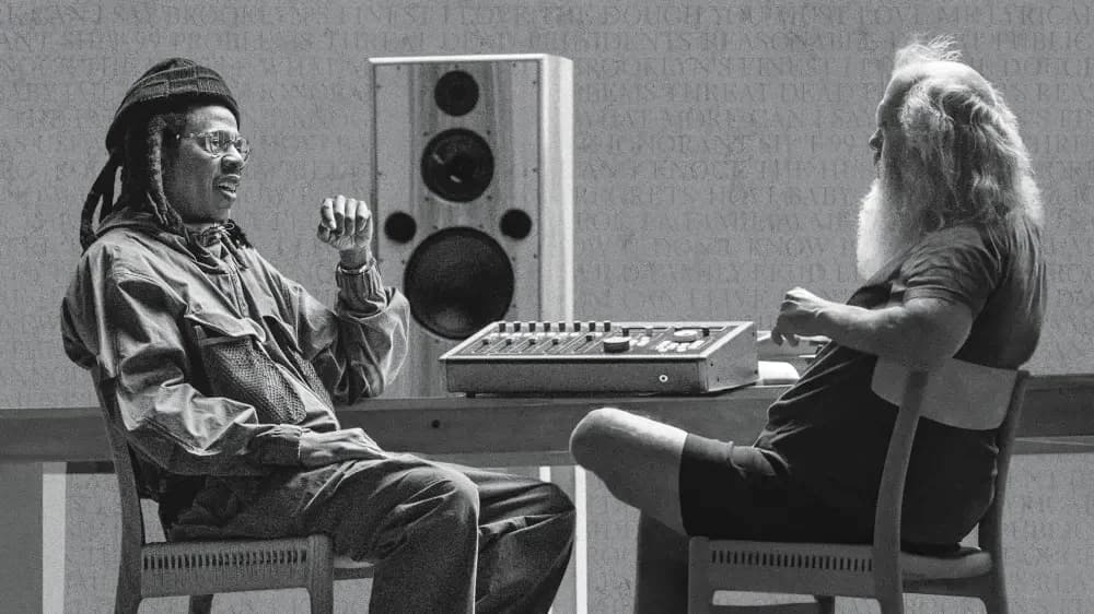 A black-and-white photograph of Jay-Z and Rick Rubin seated across from each other at a mixing desk, mid-conversation