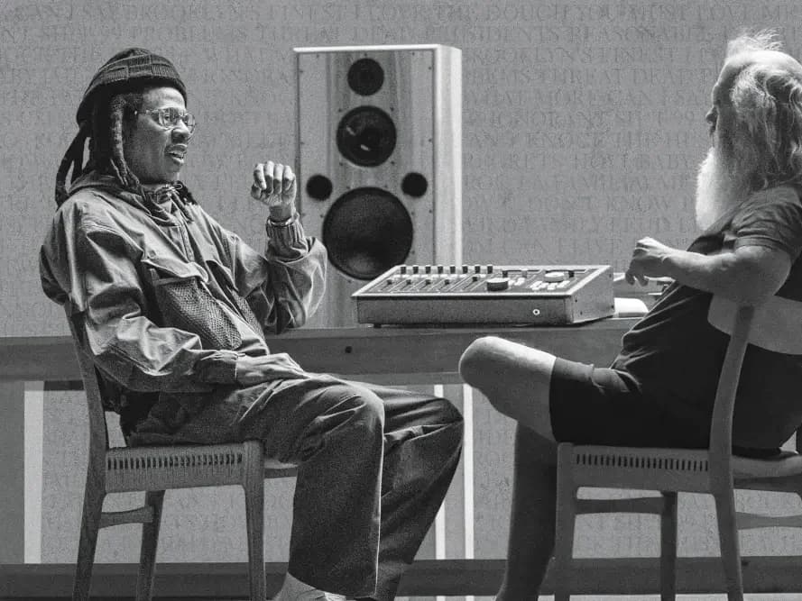 A black-and-white photograph of Jay-Z and Rick Rubin seated across from each other at a mixing desk, mid-conversation